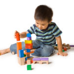 Little boy building a tower with colorful wooden blocks. Studio shot, isolated on white.